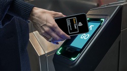 Hand holding a phone using contactless payment at a transit turnstile with a green GO indicator.